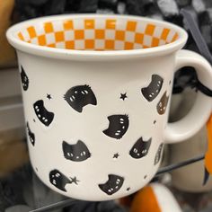 a white cup with black cats on it sitting on a table next to other items