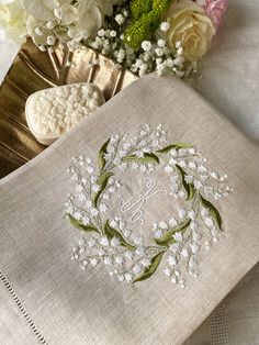 some flowers are sitting on top of a table cloth and two napkins with embroidered monogram