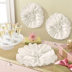 three white paper flowers are sitting on a table with champagne glasses and gift wrapped in pink ribbon