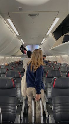 a woman is standing on an airplane with her luggage and looking out the window at other passengers