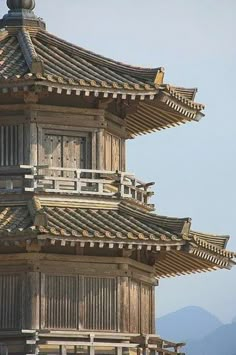 a tall wooden building with a clock on the top of it's tower and mountains in the background