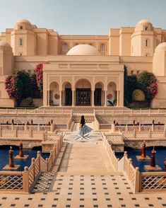 a woman standing in front of a large building with fountains and statues on the ground