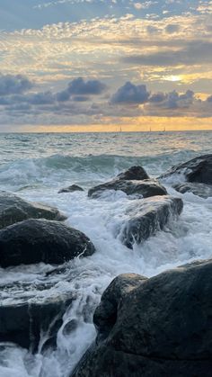 the sun is setting over the ocean with rocks in the foreground