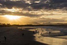 people are walking on the beach at sunset