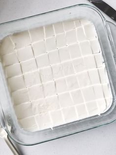 a glass dish filled with white cheese next to a knife and fork on a table