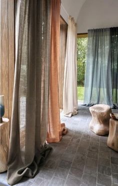 an open room with sheer curtains on the windows and wooden stools in front of them