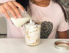 a woman pouring milk into a jar with food in it on a table next to a cup