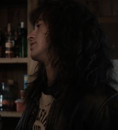 a man with long black hair standing in front of a shelf full of liquor bottles