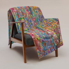 a chair with a colorful blanket on it's back and arm rests in front of a gray background