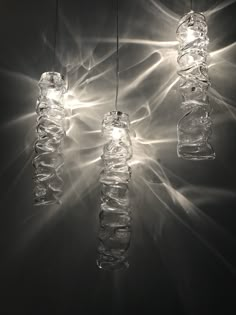 three glass bottles hanging from a ceiling with light shining through them and some lights on the wall