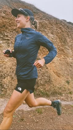 a woman running down a dirt road next to a hill