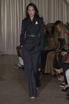 a model walks down the runway in a pinstripe suit and matching heels with her hair pulled back