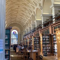 people are sitting at tables in the library with bookshelves and arched ceilinging