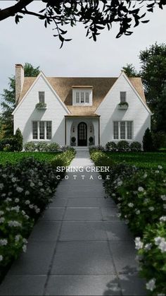 a white house surrounded by bushes and flowers with the words spring creek cottage on it