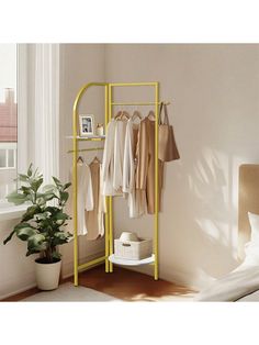 a clothes rack in the corner of a room next to a potted plant and window