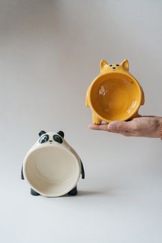 a hand holding a yellow and black cat bowl next to a small ceramic panda bear dish