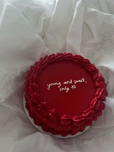 a red cake with writing on it sitting on top of a white sheet covered table