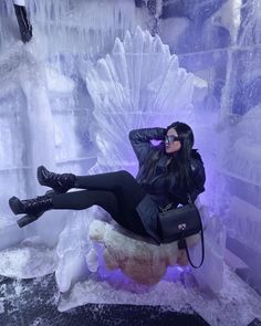 a woman in black is sitting on an ice sculpture with her legs spread out and feet up