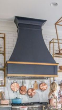 two people standing in front of an oven with copper pans hanging from the wall