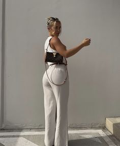 a woman in white pants and black top pointing at something with her hand on the wall