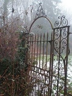 an old iron gate with snow on the ground and trees in the backround