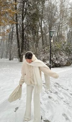 a woman standing in the snow with her scarf around her neck and wearing white pants