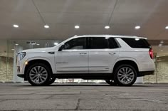 a white suv is parked in front of a large glass building with its lights on