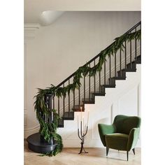 a green chair sitting in front of a stair case next to a banister with greenery on it