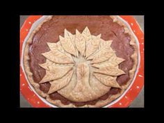 a pie with leaves on it sitting on top of a red and white tablecloth