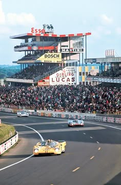 two cars driving down a race track in front of a large group of people watching