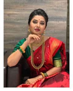 a woman in a red and green sari sitting on a couch with her hand under her chin