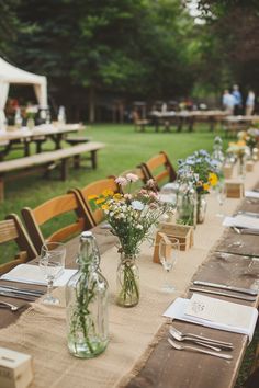 a long table is set up with flowers in vases and place settings for dinner