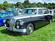 an old black car parked on top of a lush green field next to other cars