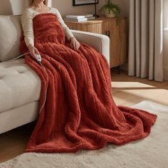 a woman sitting on a couch with a red blanket over her and holding a remote control