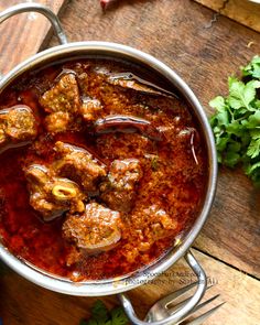 a pot filled with meat and sauce on top of a wooden table next to some parsley