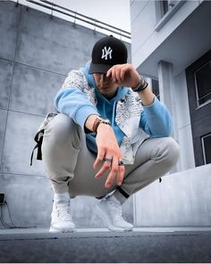 a young man wearing a new york yankees cap crouches in front of a building