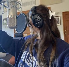 a girl wearing headphones is recording in front of a microphone