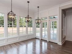 an empty living room with wood floors and large windows, chandeliers hanging from the ceiling