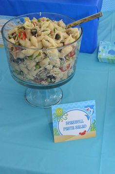 a bowl of pasta salad on a table with a blue table cloth and name tag