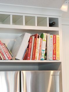 a book shelf filled with books next to a silver refrigerator freezer in a kitchen