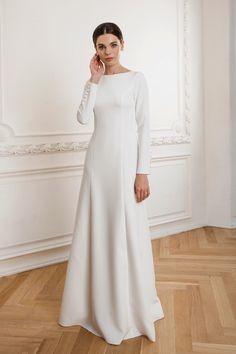 a woman in a long white dress standing on a wooden floor with her hand to her face