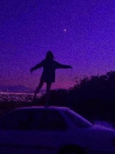 a person standing on top of a white car in the dark with their arms outstretched