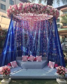 an outdoor wedding setup with blue drapes and pink flowers on the canopy, surrounded by greenery