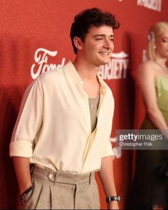 a young man standing in front of a red carpet and smiling at the camera with his hands on his hips