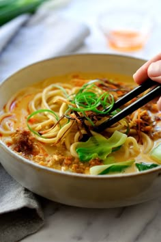 someone holding chopsticks over a bowl of noodles