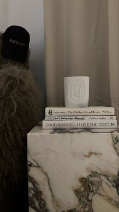 a stack of books sitting on top of a marble block next to a black and white hat