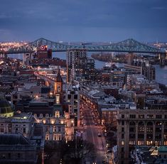 an aerial view of a city at night with the bridge in the background and lights on