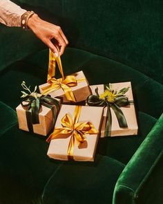 three wrapped presents sitting on top of a green velvet couch next to a person's hand