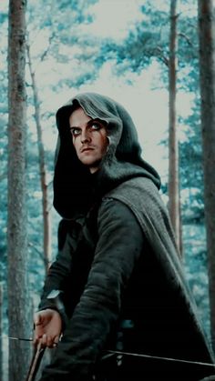 a man dressed in medieval clothing holding a bow and arrow while standing in the woods