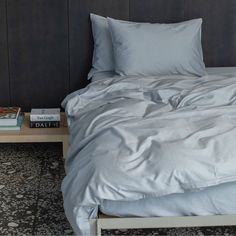 an unmade bed with two books on the side and a gray wall behind it